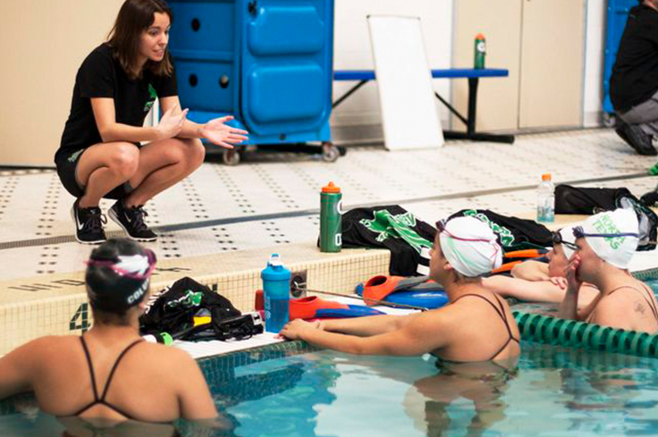 Swimming Coach discussing performance techniques with athlete swimmers in pool